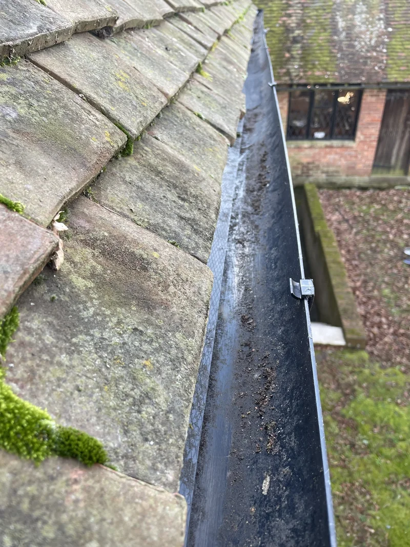 Open gutter channel beneath weathered roof tiles with scattered residue